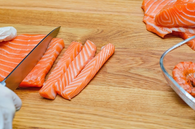 Chef's hands close up. On a wooden cutting board, the chef cuts a red fish with a knife. Salmon for Japanese sushi