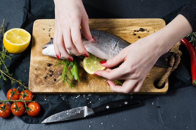 The chef's hands stuffed Dorado fish on a wooden chopping Board with parsley and cilantro. 