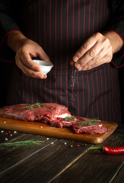 The chef salts the meat before frying or roasting Fresh veal on the kitchen table