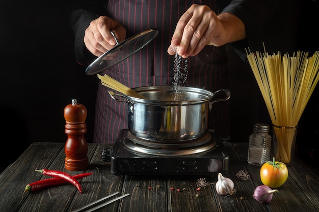 The chef salts organic pasta in a hot pot in the kitchen Delicious hotel food recipe Traditional Italian cuisine