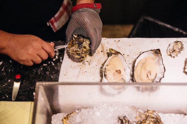 Chef shucking a fresh oyster with knife and stainless steel mesh oyster glove.