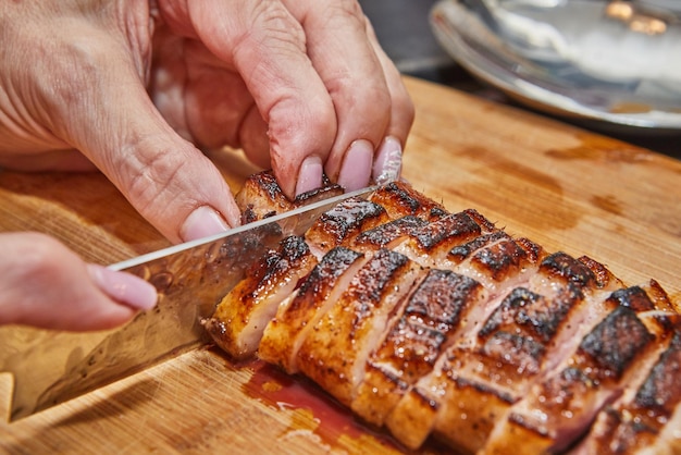 Chef slices the finished duck breast after frying on wooden board for serving