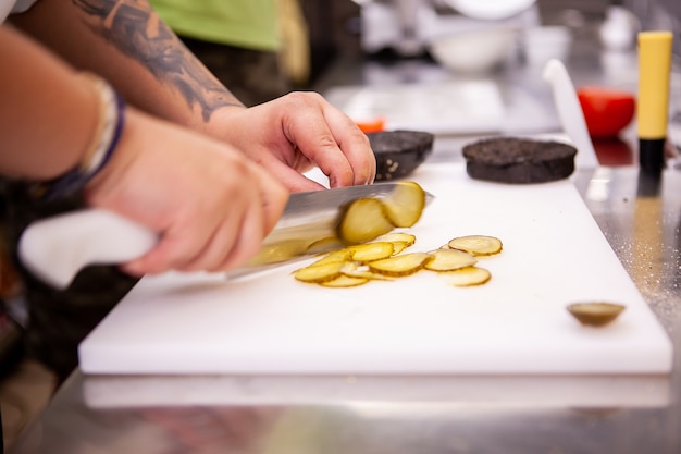 Chef slices pickles for delicious burger in restaurant. Food preparation