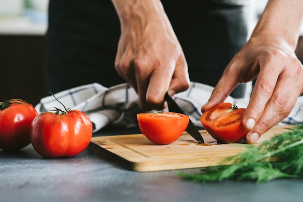 Chef slicing tomato using knife on the table in home