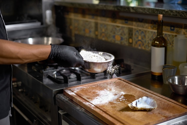 The Chef sprinkles flour Fresh Oysters for Roasting in the kitchen, 