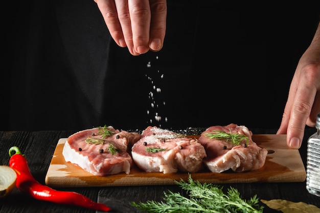 The chef sprinkles the meat with salt. Preparing meat before baking. Working environment in the kitchen of a restaurant or cafe