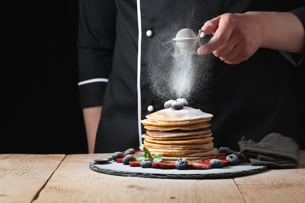 The chef sprinkles powdered sugar on the pancakes.