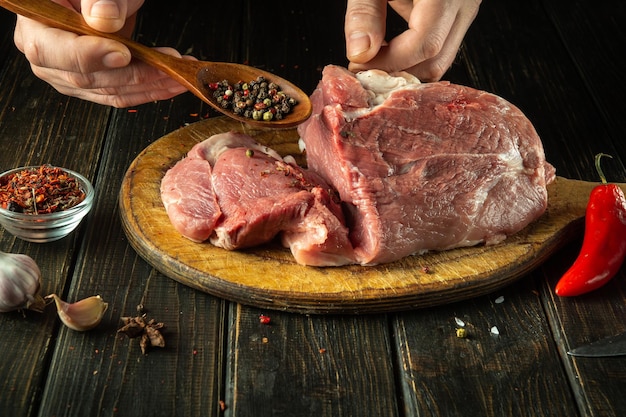 The chef sprinkles raw meat with dry pepper Preparing beef meat before roasting