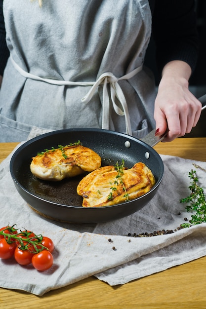 Chef sprinkles thyme on chicken Breasts in a frying pan. 