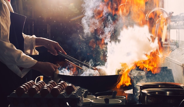 Chef stir fry busy cooking in kitchen. Chef stir fry the food in a frying pan, smoke and splatter the sauce in the kitchen.
