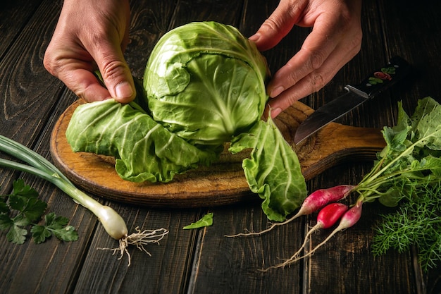 The chef strips leaves from the fresh cabbage on cutting board before preparing a vegetarian dish