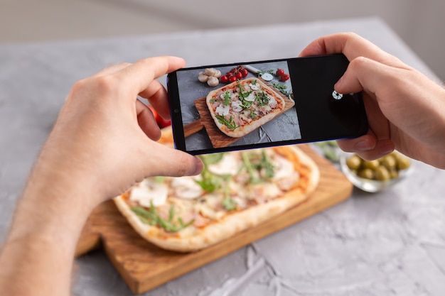 Photo chef takes pictures of the cooked of italian pizza with parma ham on smartphone photographing food