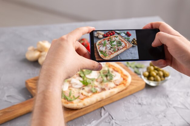 Photo chef takes pictures of the cooked of italian pizza with parma ham on smartphone photographing food