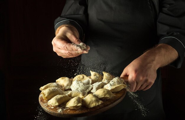 The chef throws flour to raw dumplings on a cutting kitchen board before cooking Black space for menu or recipe