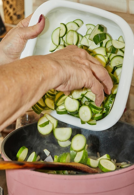 Chef tosses sliced zucchini into frying pan on gas stove to prepare the dish