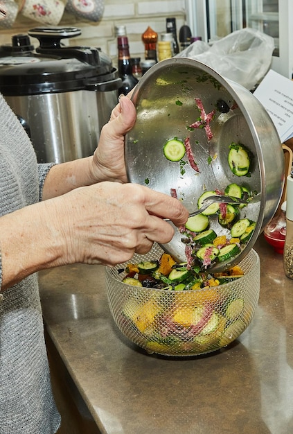 Chef transfers the Salad with zucchini oranges and salami from the bowl to the salad bowls French gourmet cuisine on wooden background