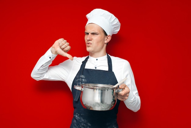 Chef in uniform holds a bad dish and shows dislike on a red isolated background bad smell concept