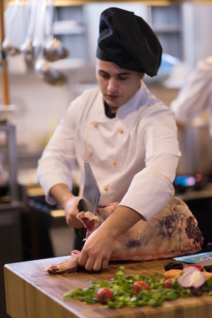 chef using ax while cutting big piece of beef  on wooden board in restaurant kitchen