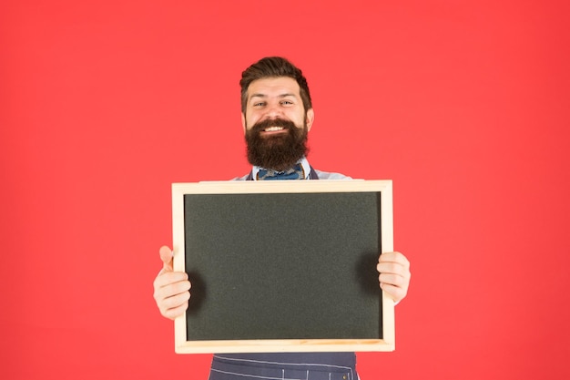 Chef with blackboard copy space Advertising place Store sale Black friday discount Advertising concept Cooking meal by recipe Happy hours Cafe shop advertising Man bearded hipster in apron