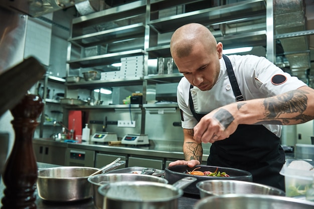 chef with several tattoos on his arms garnishing pasta carbonara in a restaurant kitchen