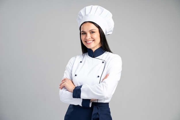 Chef woman wearing uniform and cap standing arms crossed and posing over isolated grey background. Occupation concept