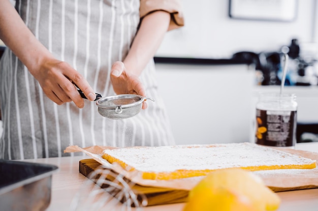 Chefs hands with small sieve for baking Baker decorating and sprinkling orange cake or pie with powdered sugar Kitchen background homemade and handmade bakery goods