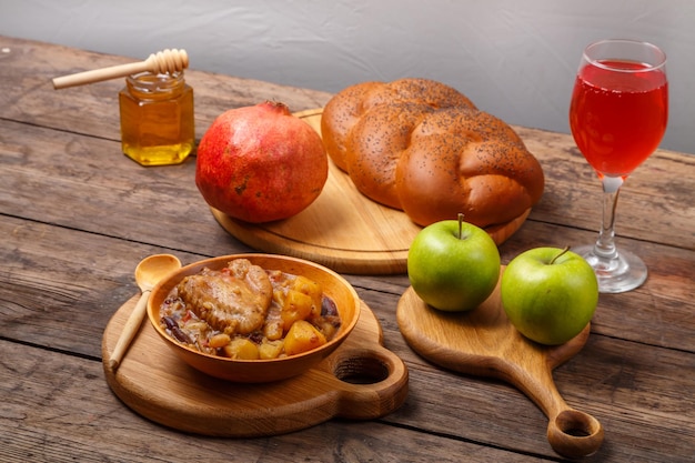 Chelnt with chicken in a wooden plate on the festive table for Rosh Hashanah next to challah honey and apples