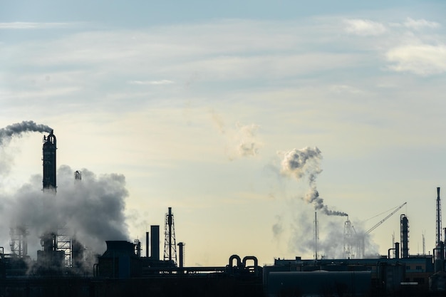 Photo chemical industry environmental pollution by harmful emissions into the atmosphere poisonous smoke comes from the big pipes the factory poisons nature silhouette of pipes and smoke sunny day