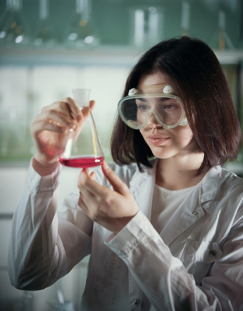 Chemical laboratory young woman in work glasses looking at the flask