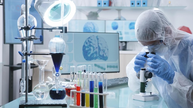 Chemist researcher doctor with ppe equipment analyzing dna sample using microscope during medical experiment in chemistry laboratory. Scientist man developing vaccine to prevent infection with covid19