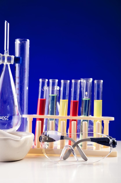 Chemistry lab set on a table with protective eyeglasses over blue background. Glassware and biology equipment