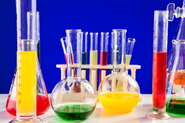 Chemistry lab set with colored liquids on a table over blue background. Glassware and biology equipment