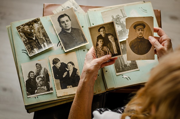 Cherkasy/Ukraine- December 12, 2019: Female hands holding and old photo of her relatives. Vintage photo album with photos. Family and life values concept.