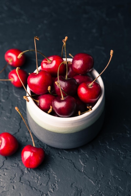 Cherries in a bowl on a black background Sweet fresh red cherries in ceramic bowl on black stone background Fruits healthy food