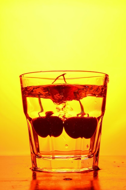 Cherries in a glass on a toned background A bunch of fresh ripe cherries falling into a glass of water with bubbles closeup Refreshing cocktail concept