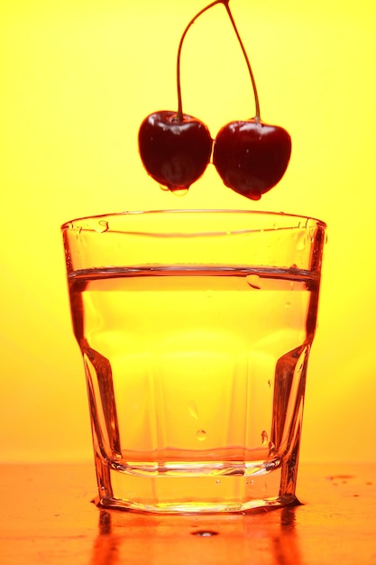 Cherries in a glass on a toned background A bunch of fresh ripe cherries falling into a glass of water with bubbles closeup Refreshing cocktail concept