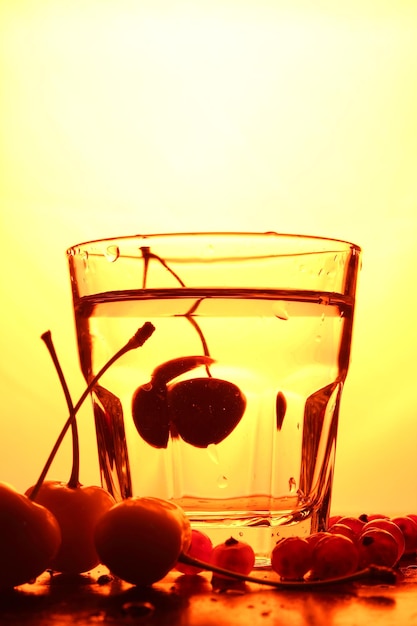 Cherries in a glass on a toned background A bunch of fresh ripe cherries falling into a glass of water with bubbles closeup Refreshing cocktail concept