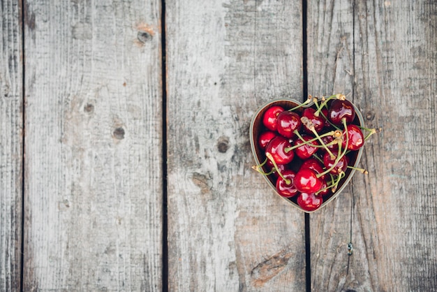 Cherries in a heart-shaped bowl on a rustic wooden surface