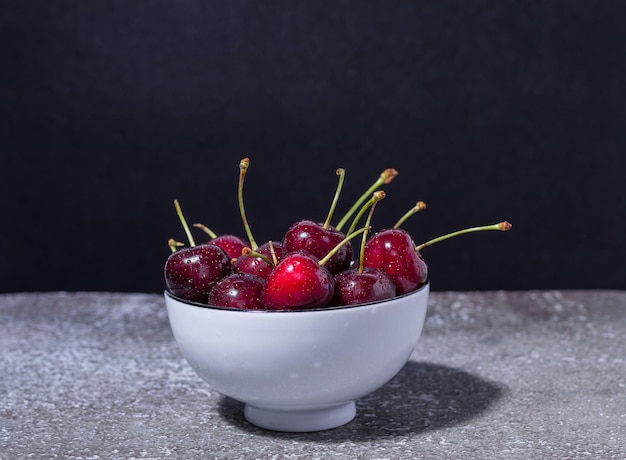 cherries in white bowl on the table and black background