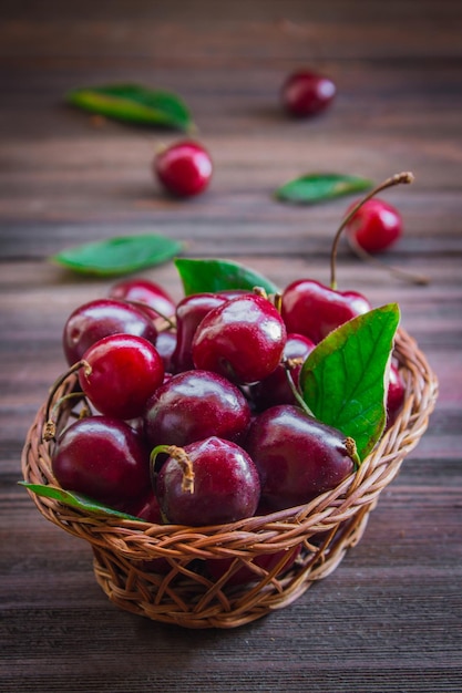 Cherries with leaves in a basket on a wooden background