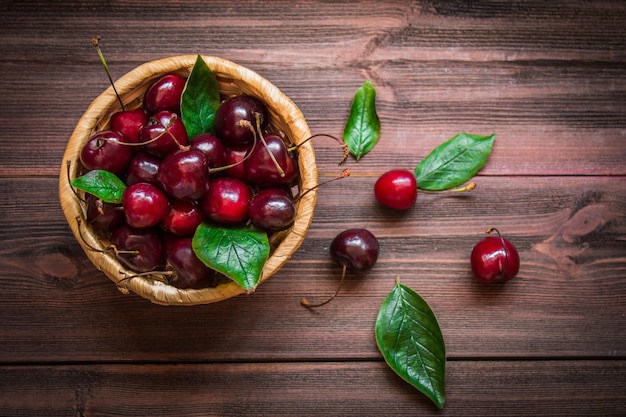 Cherries with leaves in a basket on a wooden background