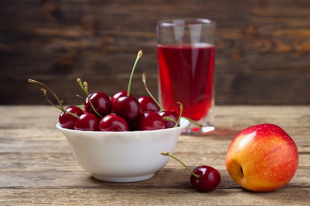 Cherry, apple and a glass of juice on a wooden table