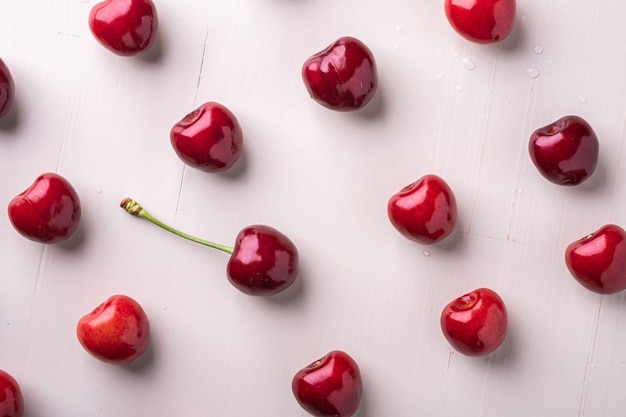 Cherry berries with one cherry with stem pattern macro texture on wooden white background and water drops top view