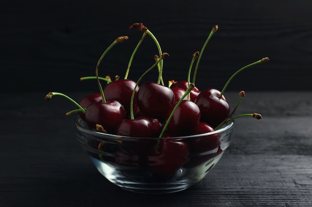 Cherry in a glass plate on a black wooden background