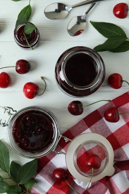 Cherry jam and ingredients on white wooden table