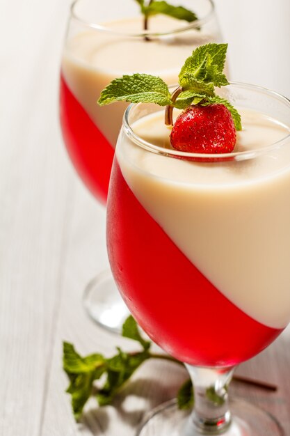 Cherry and milk jelly in the glasses topped mint leaves and strawberry pieces on the wooden background