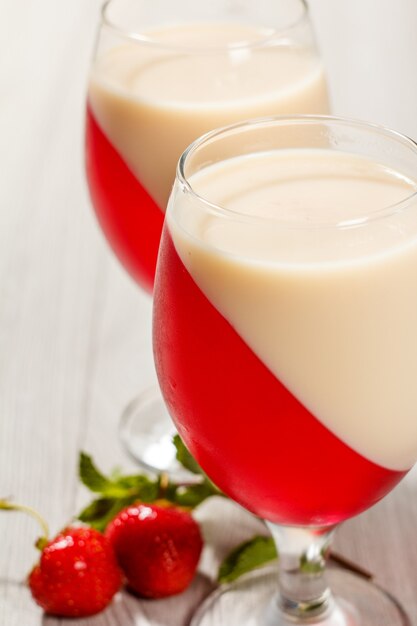 Cherry and milk jelly in the glasses with mint leaves and strawberries on the background