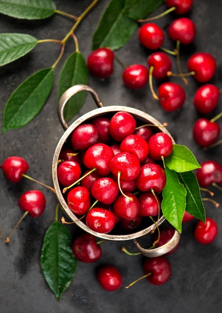 Cherry summer background A large number of cherries with leaves on the table in a saucepan on a black background