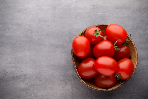 Cherry tomatoes. Three cherry tomatoes in a wooden bowl on a gray background.