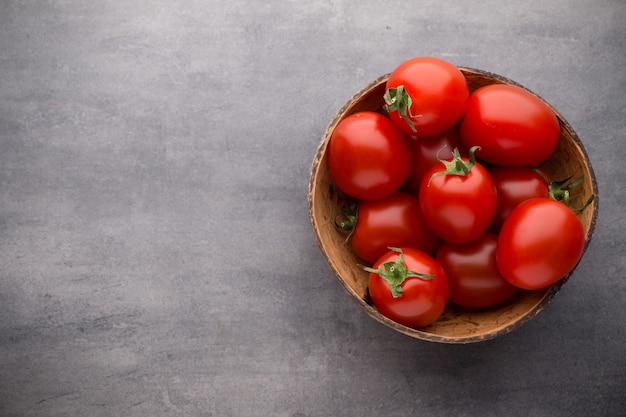 Cherry tomatoes. Three cherry tomatoes in a wooden bowl on gray.